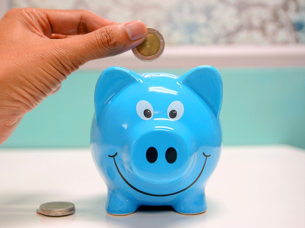 A hand inserting coins into a piggy bank